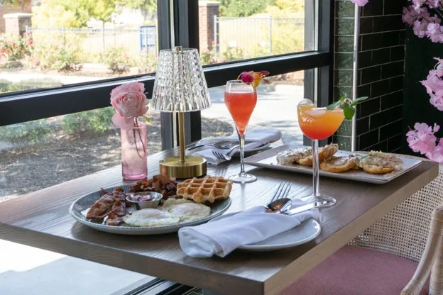 A breakfast table at Bloom Room with waffles, eggs and bacon, and two brunch cocktails