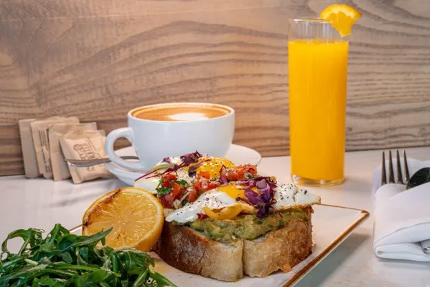 Hipster Toast with avocado mash and eggs, served with a latte and fresh orange juice